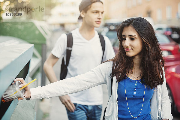 Female teenager putting disposable glass in garbage bin