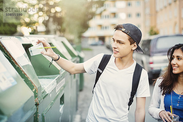 Teenager putting disposable glass in garbage bin on street