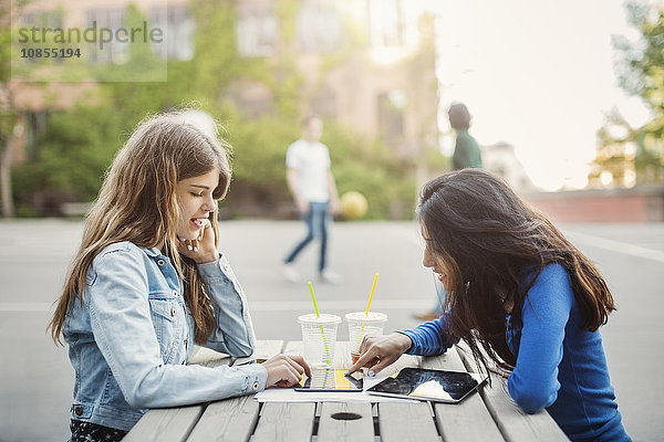 Side view of female teenagers using digital tablet at table outdoors