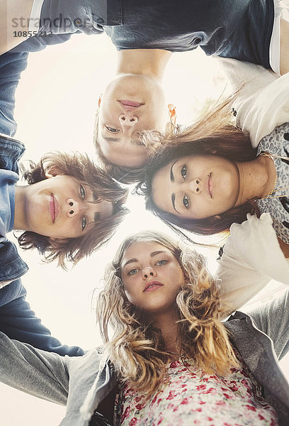 Directly below portrait of teenagers forming huddle against sky