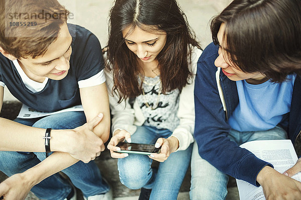 High angle view of girl using smart phone while sitting with male friends on steps