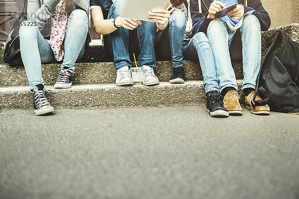 Low section of teenagers using digital table on steps