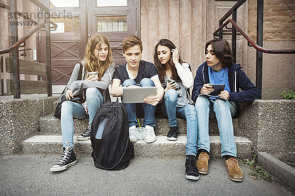 Teenagers using digital tablet while sitting on steps outdoors