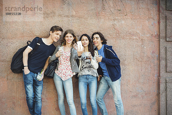 Happy teenagers taking selfie against wall