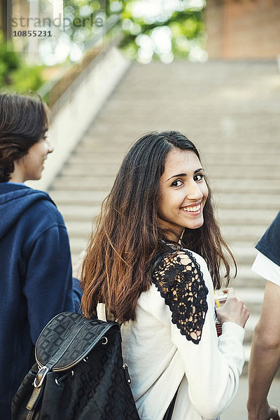 Rear view portrait of happy female teenager with male friends outdoors