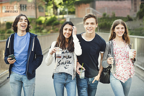 Portrait of happy teenagers holding disposable glasses and smart phones on bridge