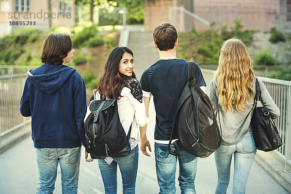 Rear view portrait of smiling teenager walking with friends on bridge