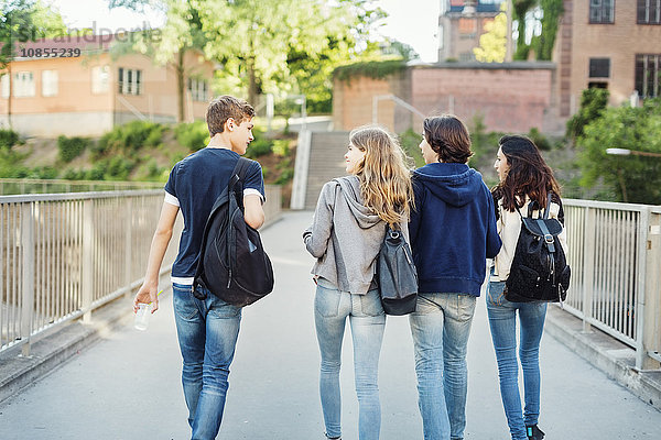 Rear view of teenagers talking while walking on bridge in city