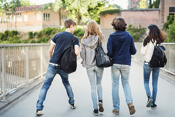 Rear view of teenagers walking on bridge in city