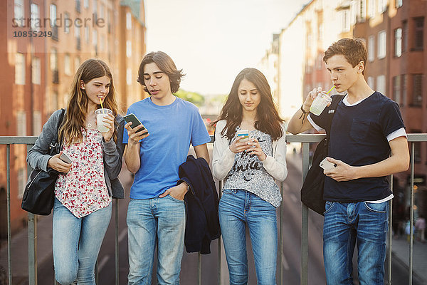 Teenagers using smart phone while drinking juice on bridge in city