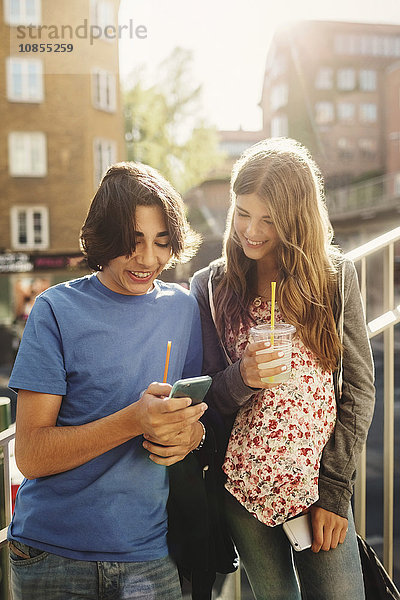 Happy teenagers using smart phone on steps in city