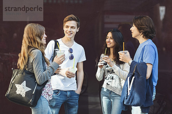 Happy teenage friends talking while holding drinks outdoors