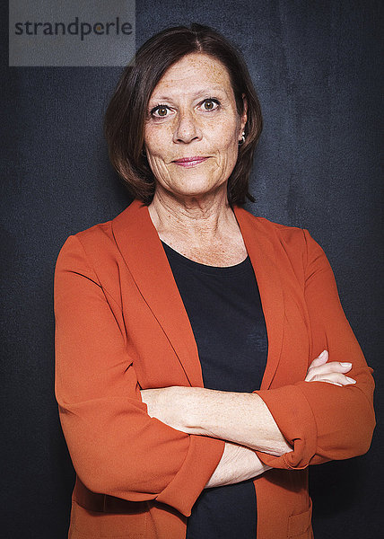 Portrait of happy mature businesswoman standing arms crossed against wall