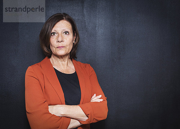 Portrait of mature businesswoman standing arms crossed against wall