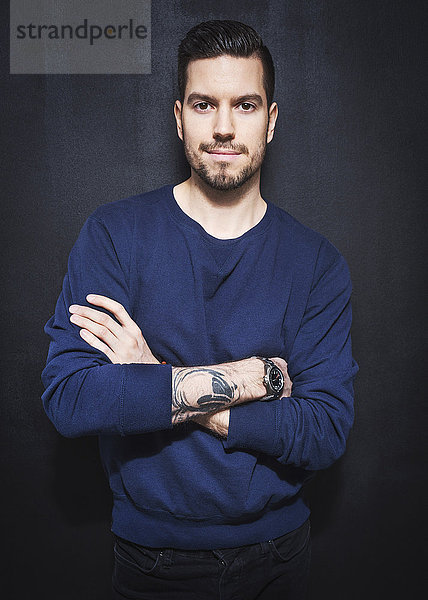 Portrait of mid adult businessman standing arms crossed against wall