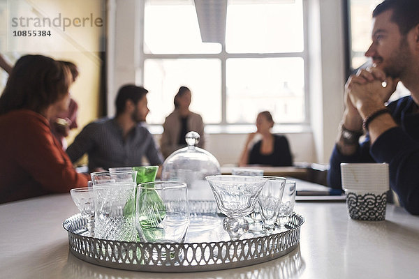 Empty drinking glasses in tray with business people discussing at conference table