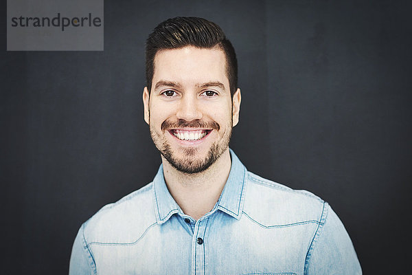 Portrait of smiling mid adult businessman standing against wall in office