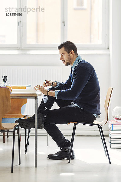 Full length side view of businessman with book at desk in office