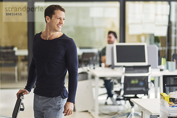 Happy mid adult businessman looking away with colleague in background at office