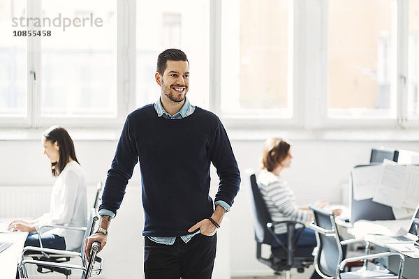 Happy mid adult businessman with colleagues working in background at office