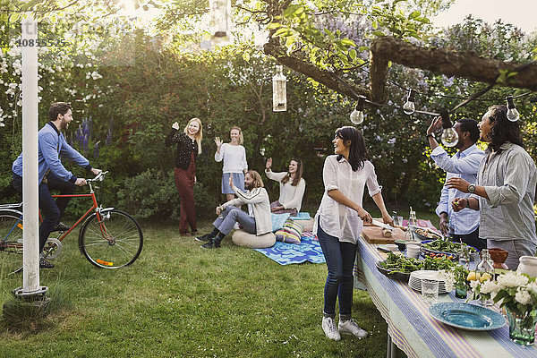 Multi-ethnic people greeting friend riding bicycle in yard during summer party