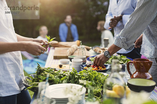 Midsection of friends preparing food at dining table in backyard