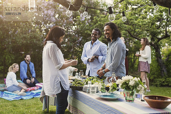 Multi-ethnic friends preparing food at dining table in backyard