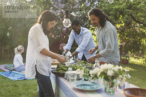 Friends preparing food at dining table in backyard during summer party