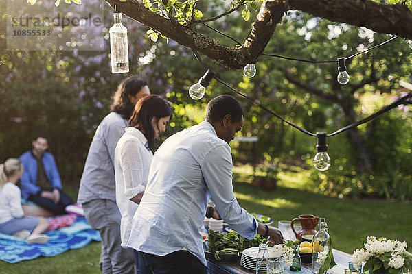 Friends preparing food at table in yard during summer party