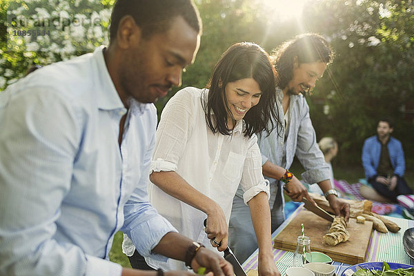 Happy young woman with male friends preparing food in backyard during summer party