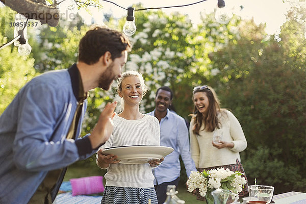 Happy young woman holding plate while enjoying summer party with friends in yard