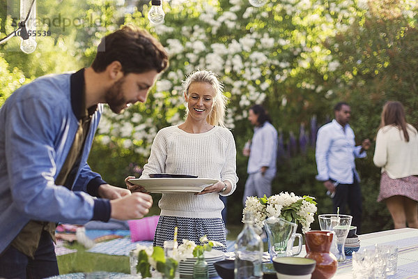 Happy young woman holding plates while enjoying summer party with friends in yard