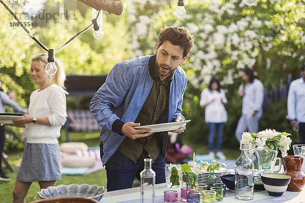 Young man holding empty plate at dining table in backyard during summer party