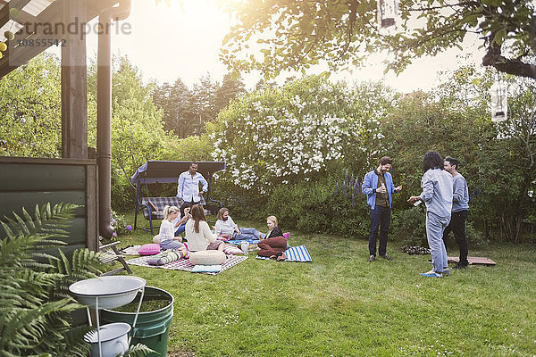 Multi-ethnic friends gossiping while having food in lawn during summer party