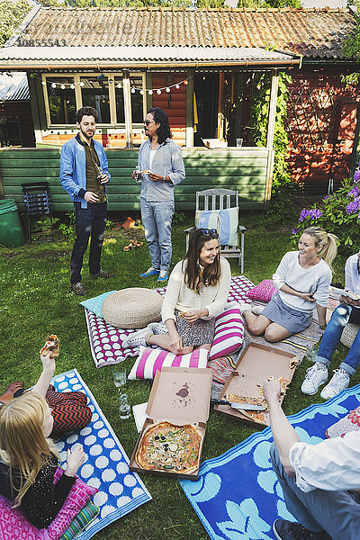 Happy multi-ethnic friends having pizza in lawn during summer party