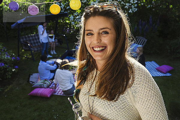 Portrait of happy young woman with friends in background at yard during summer party