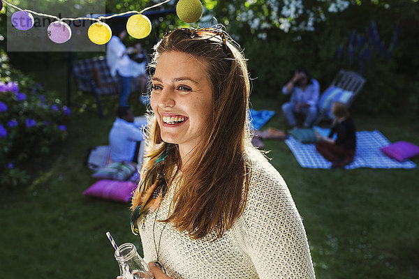 Happy young woman with friends in background at yard during summer party