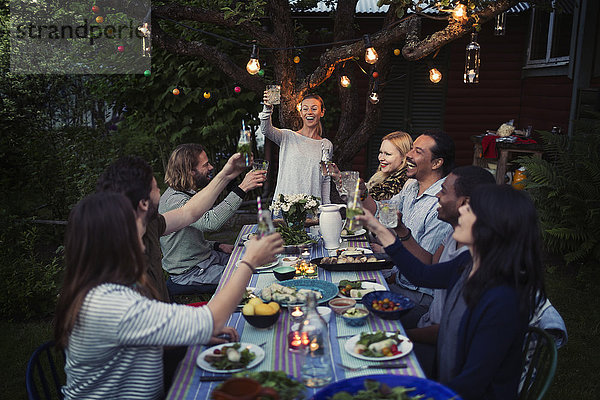 Happy woman toasting drink to friends at dining table while enjoying outdoor dinner party