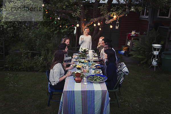 Happy woman standing at dining table with friends enjoying dinner party at yard