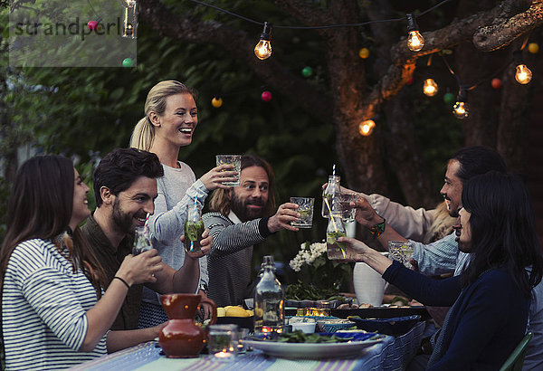 Multi-ethnic friends toasting drinks at dinner table in yard