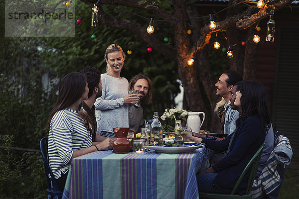 Happy woman talking to friends sitting at dinner table in yard