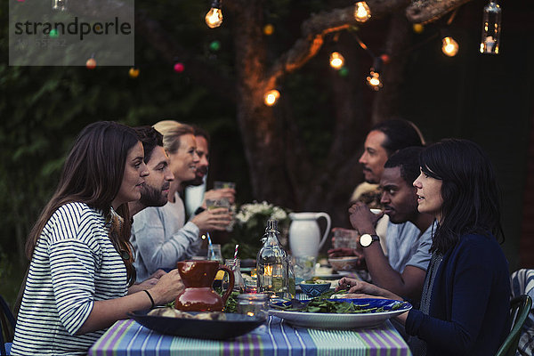 Side view of happy multi-ethnic friends having dinner at table in yard