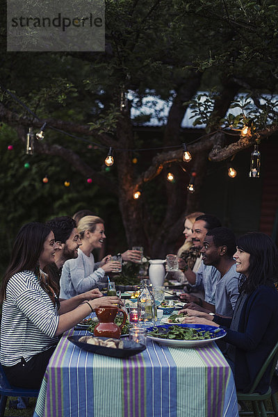 Side view of happy friends having dinner at table in yard