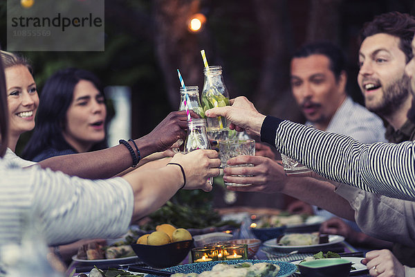 Happy friends toasting mojito glasses at table during dinner party in yard