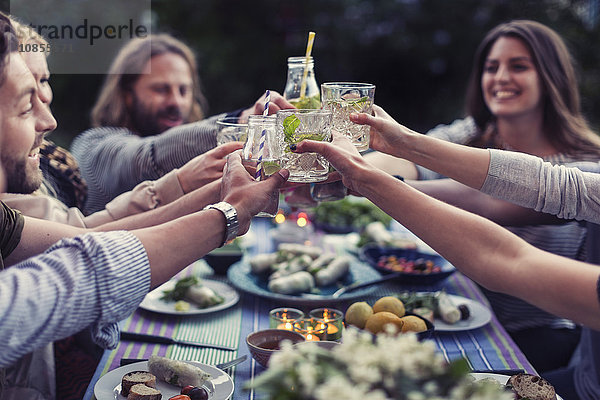 Happy friends toasting mojito glasses at dinner table in yard