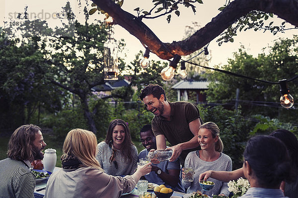 Happy man serving water to friend during dinner party at yard