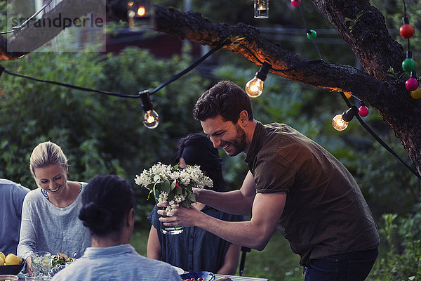 Happy man holding flower vase while enjoying dinner party with friends at yard