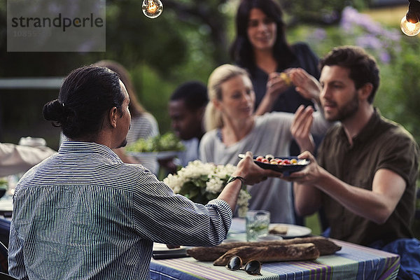 Men passing food at dining table during dinner party at yard