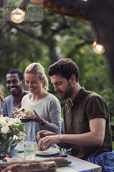 Happy woman holding bread bowl while enjoying dinner party with friends