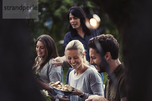 Happy woman holding bread bowl while enjoying dinner party with friends at yard